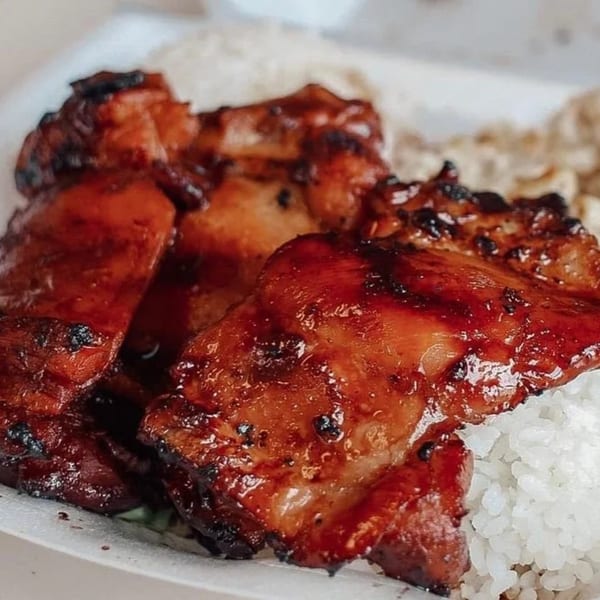 Close-up of glistening, dark red Hawaiian BBQ chicken pieces served with white rice.