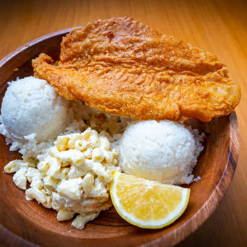 Crispy fried fish, two scoops of white rice, macaroni salad, and a lemon wedge in a wooden bowl.