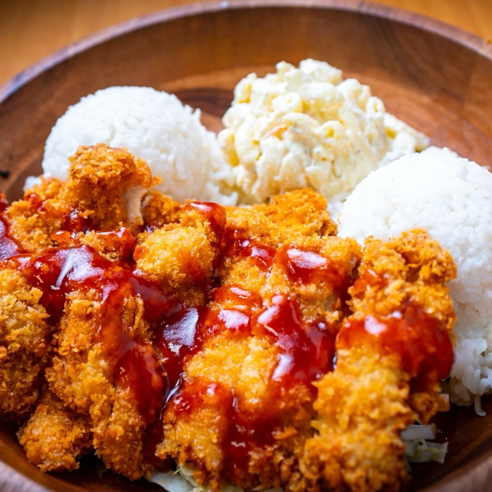 Crispy fried chicken with red sauce, white rice, and macaroni salad in a wooden bowl.