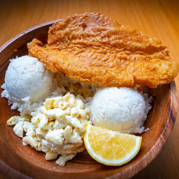 Crispy fried fish, two scoops of white rice, macaroni salad, and a lemon wedge in a wooden bowl.