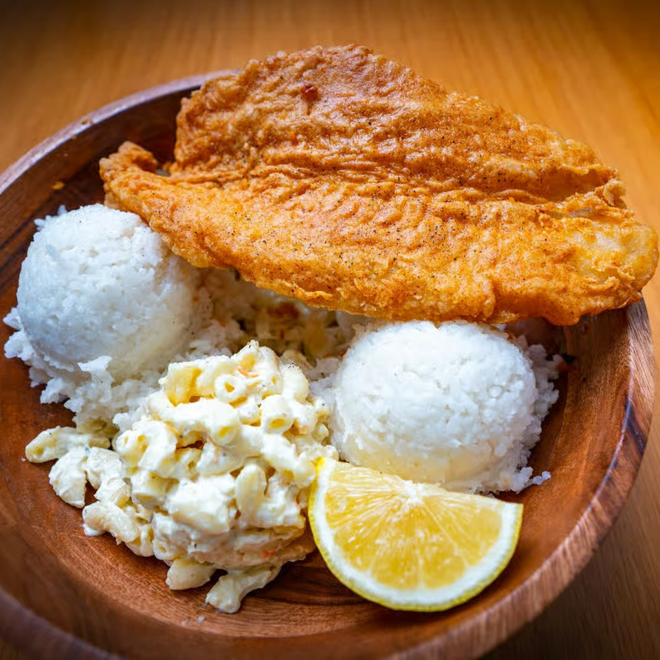 Crispy fried fish, two scoops of white rice, macaroni salad, and a lemon wedge in a wooden bowl.